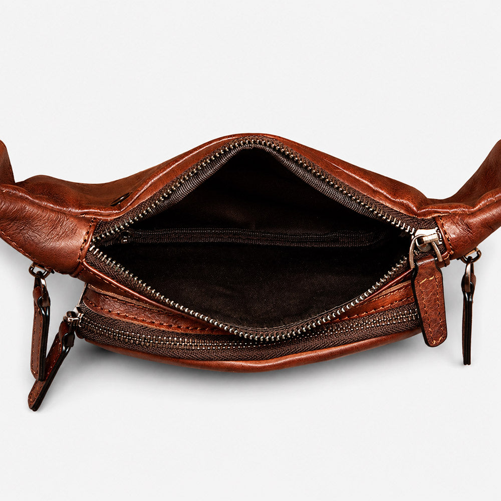 Open interior of leather waist bag showing main compartment, slip pocket, zip divider pocket, and space for phone, wallet, and keys